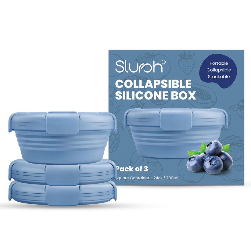 Three stacked blue Slursh collapsible silicone boxes on a warm kitchen table beside a brass thali with food.
